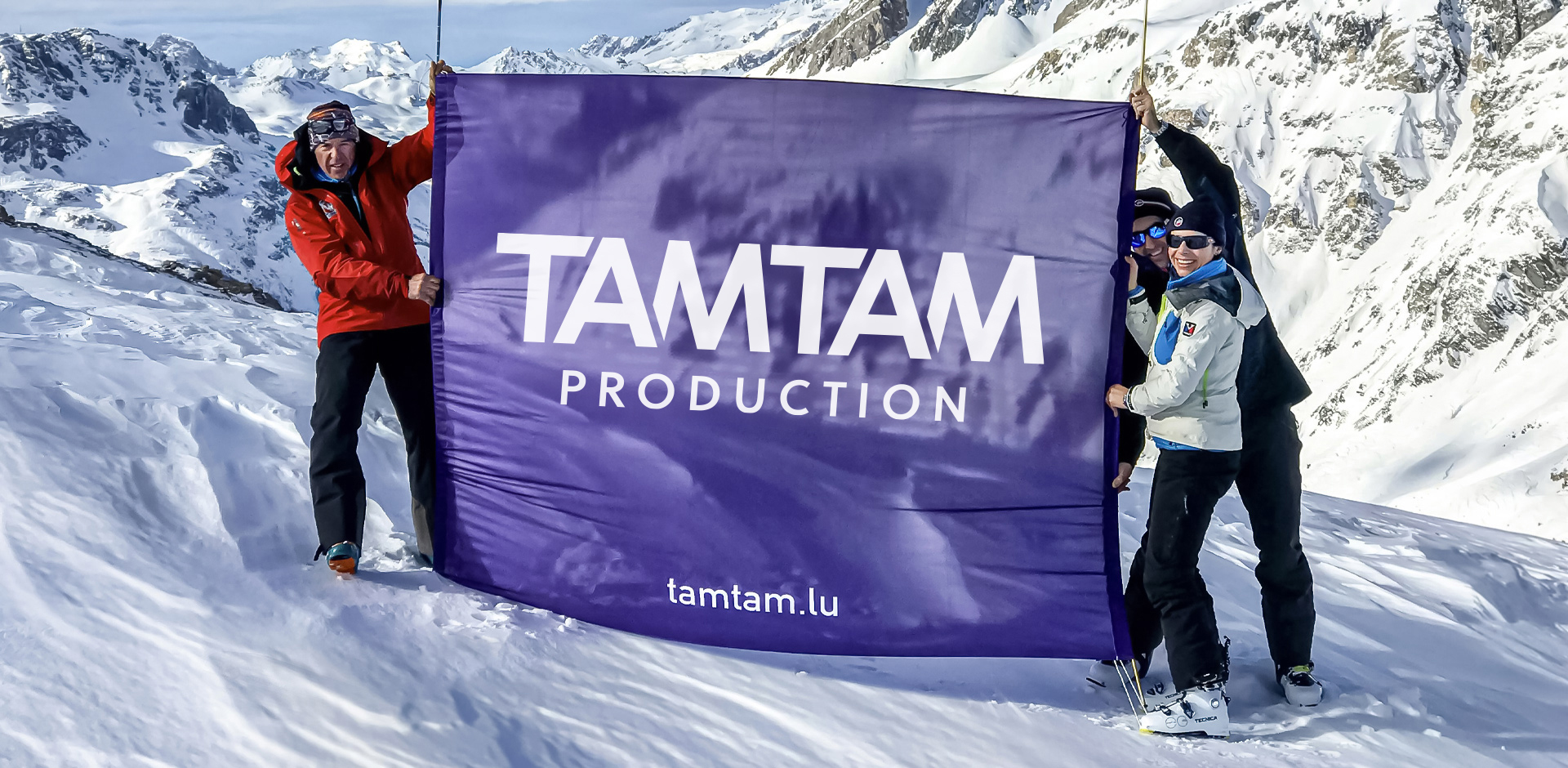 3 personnes tiennent le drapeau TAM TAM au sommet de la montagne